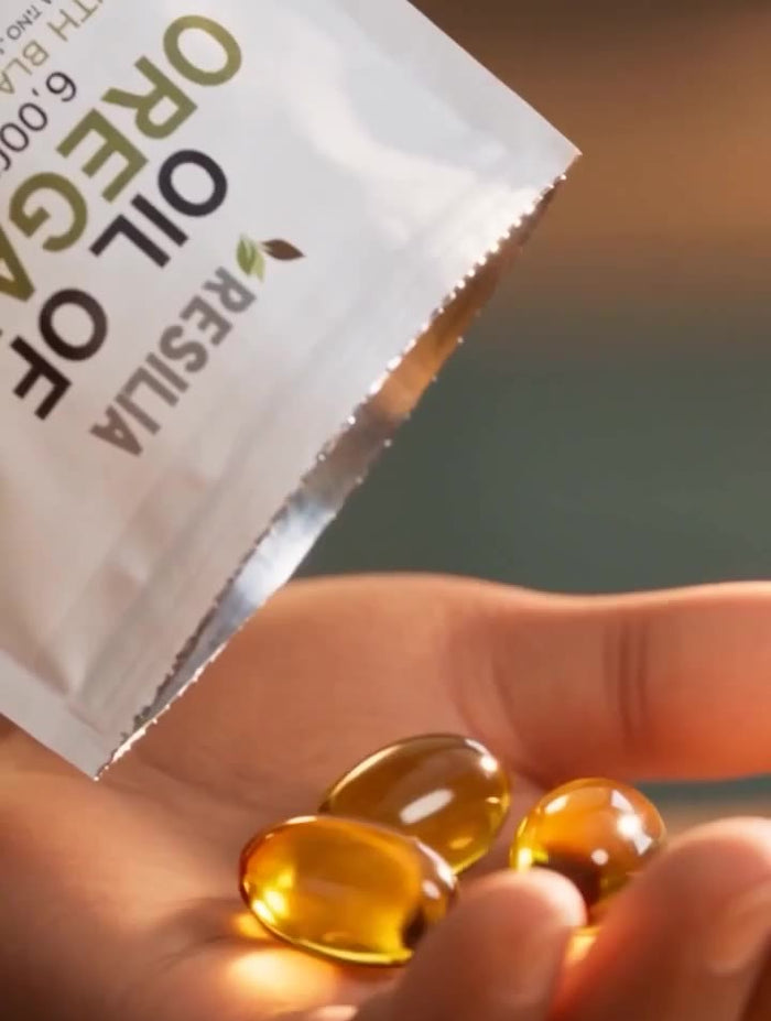 Two golden Resilia softgels in a hand