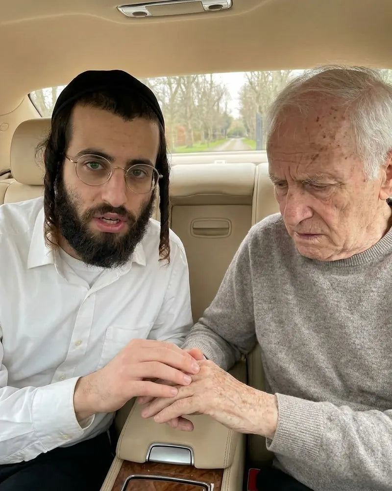 The man from the video pressing on an older man's hand in the car