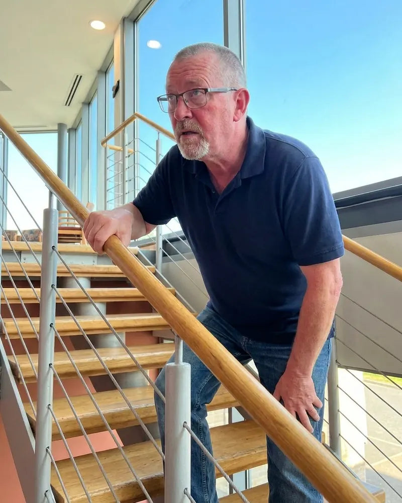 A man in his late fifties stopped halfway up a staircase, hand on the rail